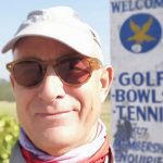 Image of James Roth, smiling, in ball cap and sunglasses, outside in front of a"Golf, Bowls, & Tennis Club" sign.